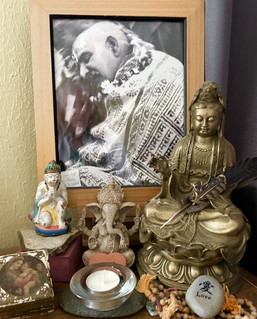 An altar with a large photo of Neem Karoli Baba, a statue of Kwan Yin, and other items, including a small old box with an image of madonna and child.